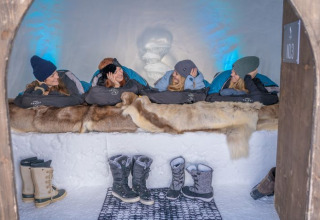 Vier personen relaxen in slaapzakken op pelzen in Iglo Lodge Burgberg, omgeven door sneeuw.