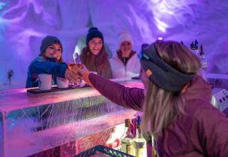 Frauen genießen Getränke an der Eisbar der Iglo Lodge Burgberg – Iglo Beieren, mit bunter Beleuchtung.