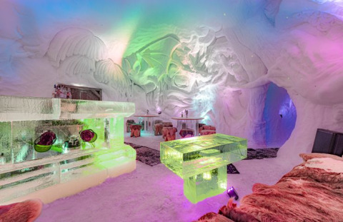 Met kleur verlichte iglokamer met ijssculpturen en bonten kleden in Iglo Lodge Burgberg, Beieren.