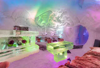 Met kleur verlichte iglokamer met ijssculpturen en bonten kleden in Iglo Lodge Burgberg, Beieren.