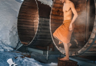 Mand træder ud af en rund træsauna iført et håndklæde, omgivet af sne ved Iglo Lodge Burgberg.