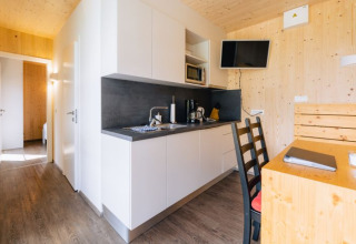 Cocina moderna y comedor de glamping lodge en Seecamping Kleblach-Lind, con paredes de madera y televisor.