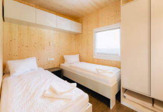 Vue intérieure d’un lodge Seecamping Kleblach-Lind avec deux lits simples, murs en bois et fenêtre.