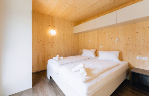 Modernes Holz-Lodge-Zimmer im Seecamping Kleblach-Lind in Kärnten mit Doppelbett und frischer Bettwäsche.