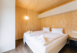 Chambre lodge moderne en bois au Seecamping Kleblach-Lind, Carinthie, avec grand lit et éclairage doux.