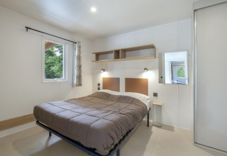 Modern bedroom with double bed, window, and shelving at Mobile home Comfort MIVA, Seasonova Camping Le Plan d’Eau.