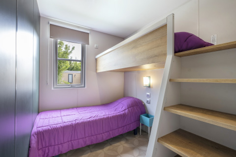 Zimmer mit Etagenbett und Einzelbett mit lila Decken, Fenster und Holztreppe in Mobile home Confort, Frankreich.