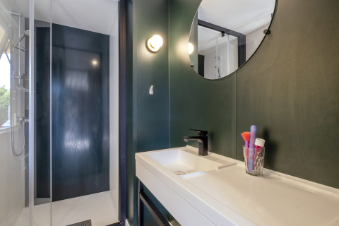 Modern bathroom with black shower, white sink, and round mirror in Mobile home Confort, France.