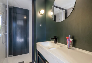 Modern bathroom with black shower, white sink, and round mirror in Mobile home Confort, France.