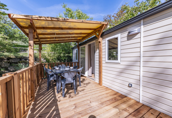 Wooden deck terrace with dining set at Static caravan Comfort with Air Conditioning, surrounded by trees.