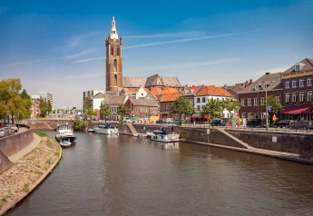 Uitzicht op een rivier met boten, historische gebouwen en een kerktoren in een sfeervolle Nederlandse stad.
