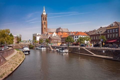 Blick auf einen Fluss mit Booten, historischen Gebäuden und einem Kirchturm in einer niederländischen Stadt.