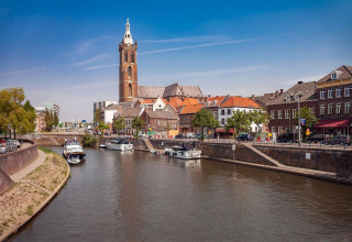 Vista de un río con barcos, edificios históricos y un campanario en el centro de una ciudad holandesa.