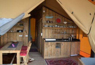 Binnenzicht van een safaritent op Inselcamping Kollersee met houten meubelen en eetruimte.