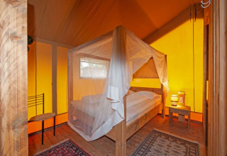 Binnenkant safaritent op Inselcamping Kollersee met hemelbed, klamboe en houten meubilair.