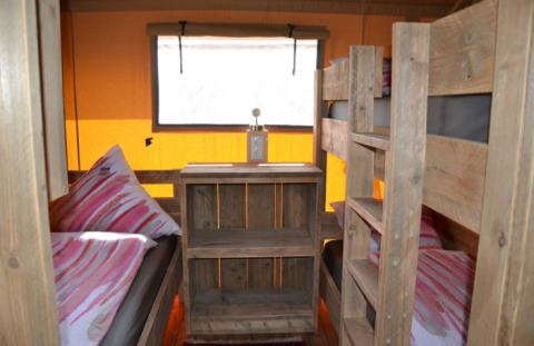 Vista interior de una tienda safari glamping en Inselcamping Kollersee con literas y muebles de madera.
