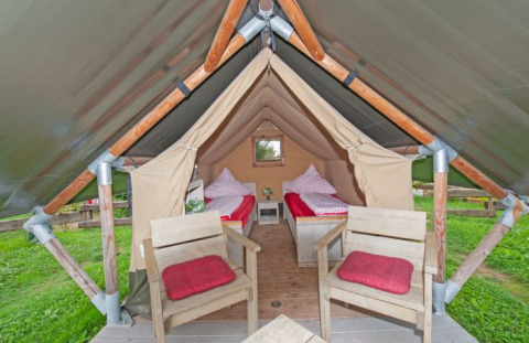 Glamping accommodatie in een safaritent bij Inselcamping Kollersee, met twee bedden en stoelen met rode kussens.