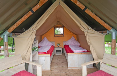 Binnenzicht van een glamping safaritent bij Inselcamping Kollersee met twee bedden en houten meubelen.