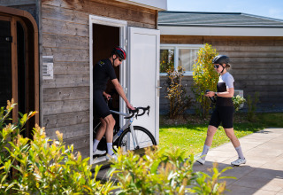 Twee fietsers met helmen bereiden zich voor bij een houten hut op een zonnige glamping-accommodatie.