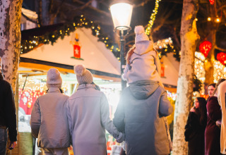 Familie schlendert gemütlich durch ein beleuchtetes Glampinggelände mit festlicher Dekoration und Lichterketten.