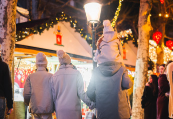 Familie nyder en hyggelig aften på et oplyst glampingmarked med boder og julelys hængende over dem.