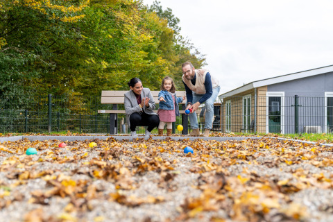 En familie hygger sig med udendørs boldspil foran deres moderne glamping-indkvartering om efteråret.