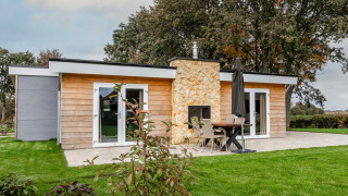 Modern garden house with wooden panels and a stone fireplace at Schaelsbergerbosch, surrounded by lawn.