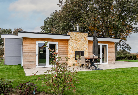 Modern garden house with wooden panels and a stone fireplace at Schaelsbergerbosch, surrounded by lawn.