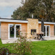 Modern garden house with wooden panels and a stone fireplace at Schaelsbergerbosch, surrounded by lawn.