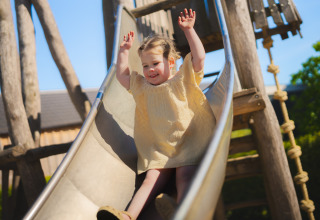 Niña deslizándose por un tobogán en el parque de un alojamiento glamping en un día soleado y alegre.