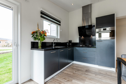 Modern kitchen with black cabinets, fresh flowers, and large windows at a lodge in Resort Mooi Bemelen.
