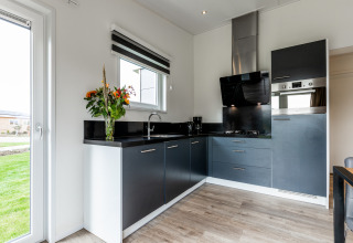 Modern kitchen with black cabinets, fresh flowers, and large windows at a lodge in Resort Mooi Bemelen.