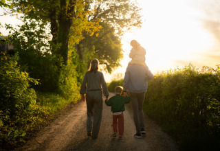 En familie går langs en skovsti ved solnedgang nær deres glamping-lejr. Natur og fællesskab.