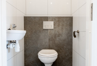 Modern restroom with wall-mounted toilet, small sink, and white tiles at Resort Mooi Bemelen in Netherlands.