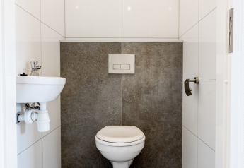 Baño moderno con inodoro suspendido, pequeño lavabo y azulejos blancos en Resort Mooi Bemelen, Países Bajos.