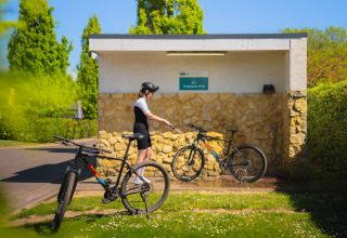 Una persona limpia una bicicleta de montaña en una estación exterior de lavado en un alojamiento glamping verde.