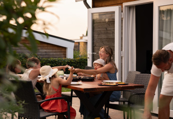 Famille partageant un dîner barbecue en plein air sur la terrasse d’un hébergement glamping moderne.
