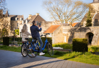 Et par holder pause fra cykeltur ved et glampingområde og tager et foto af den historiske bygning.