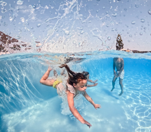 Bambini che nuotano e giocano sott'acqua in una piscina durante il glamping, con schizzi d'acqua sopra.