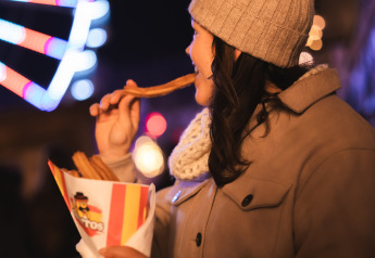 Kvinde nyder churros ved et glampingophold om aftenen, med pariserhjul og lys i baggrunden.