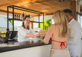Barista che sorride e serve drink a una coppia presso un bar all'aperto in una sistemazione glamping.