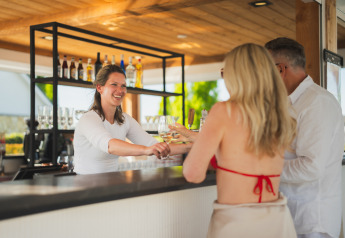 Barman serveert drankjes aan een stel bij een buitenbar op een glampingaccommodatie in de natuur.