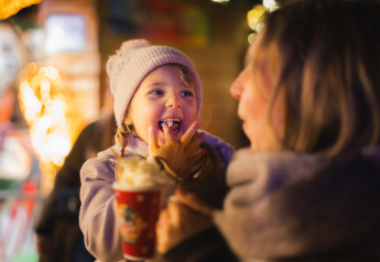 Little girl in a beanie joyfully enjoys hot chocolate and laughter with an adult at a glamping site at night.