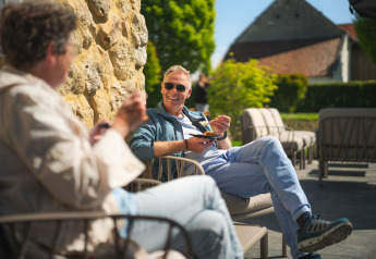 Zwei Männer genießen entspanntes Outdoor-Essen auf einer Glamping-Unterkunft bei sonnigem Wetter.