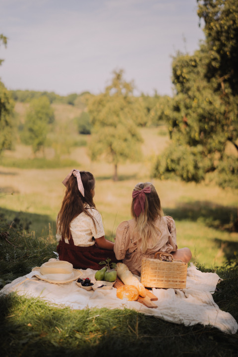 Dos mujeres disfrutan de un picnic con pan y fruta en una manta en un alojamiento de glamping en la naturaleza.