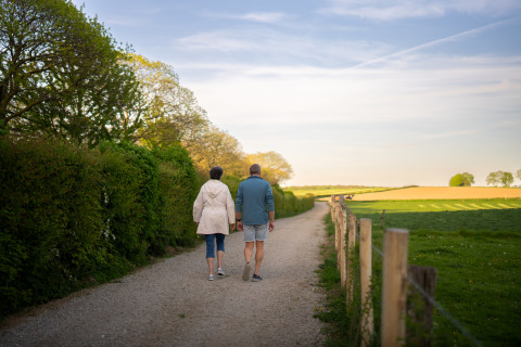 Twee personen wandelen op een gravelpad langs een veld bij een charmante glampingaccommodatie buiten.