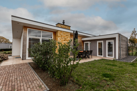 Moderne lodge met grote ramen en terras in een groene tuin bij Ravenbosch, met open haard en hot tub.
