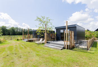 Tiny House moderne avec terrasse, transats et clôture en bois dans un cadre champêtre verdoyant.