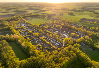 Vue aérienne d’un site de glamping entouré de bois et champs au coucher du soleil, idéal pour se ressourcer.