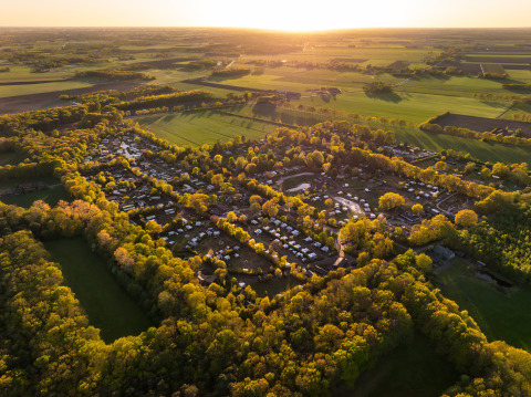 Luftaufnahme eines Glamping-Platzes, umgeben von Bäumen und Feldern, bei Sonnenuntergang auf dem Land.